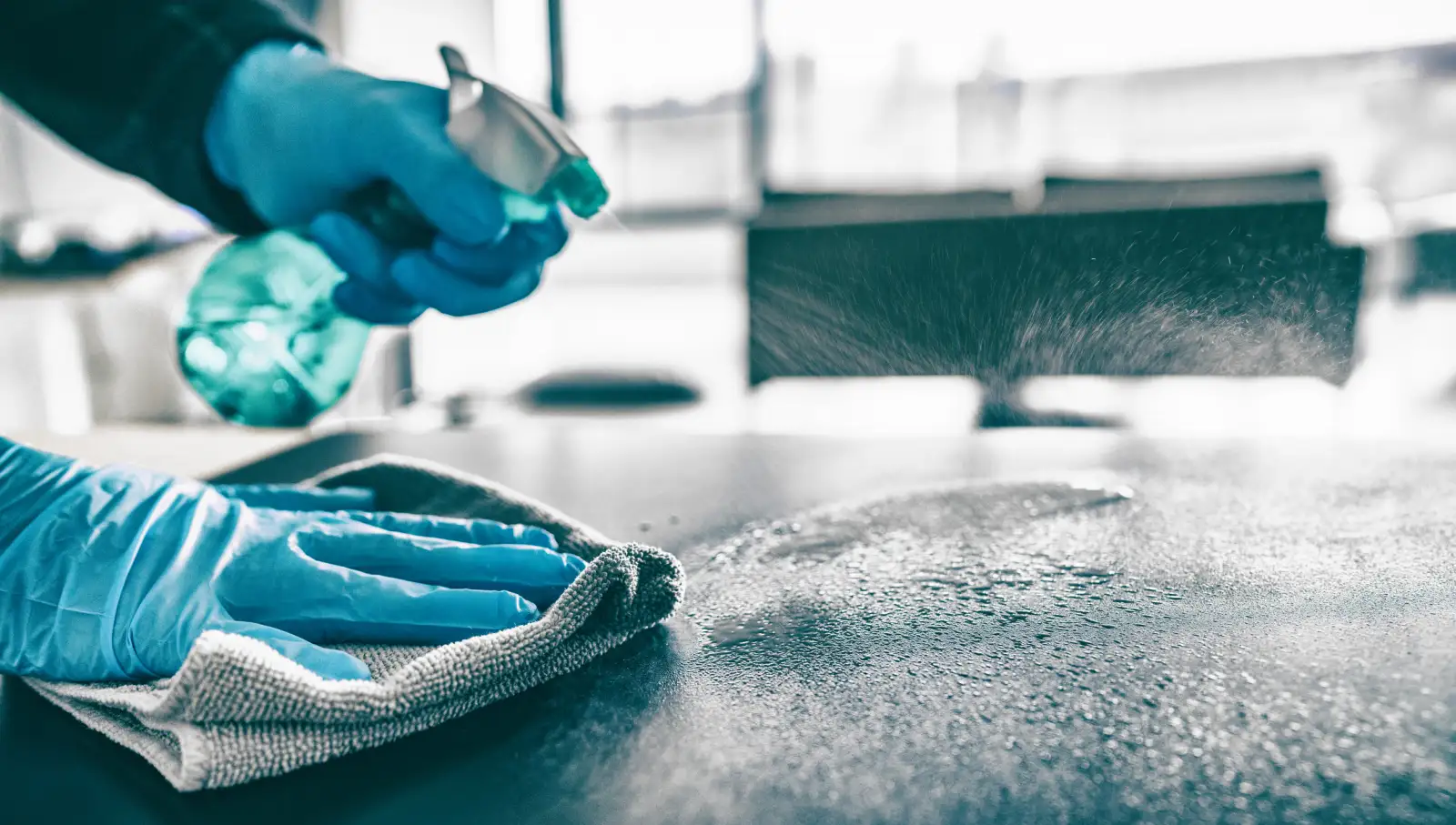 A person spraying and wiping their kitchen counter wearing blue latex gloves.