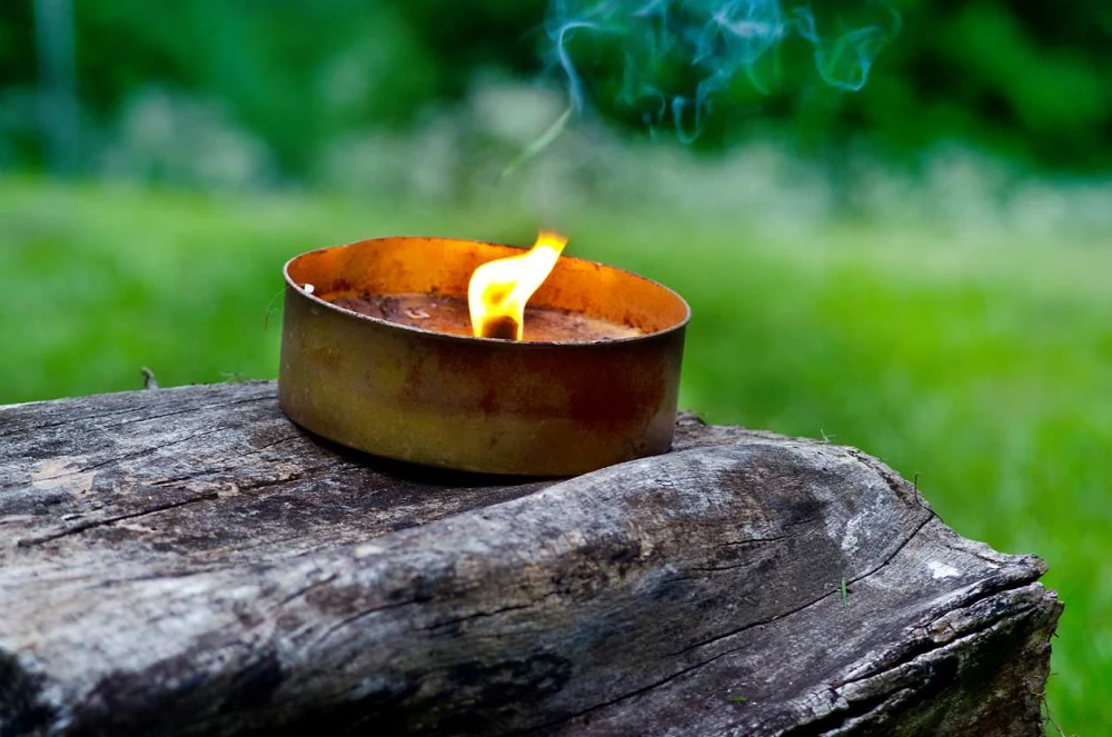 A citronella candle burning on top of a piece of wood