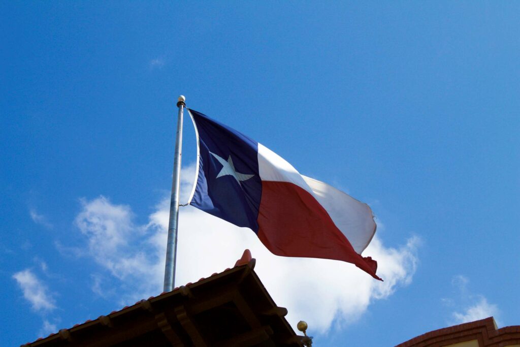 A Texas flag is waving on a pole above the roof of a house.